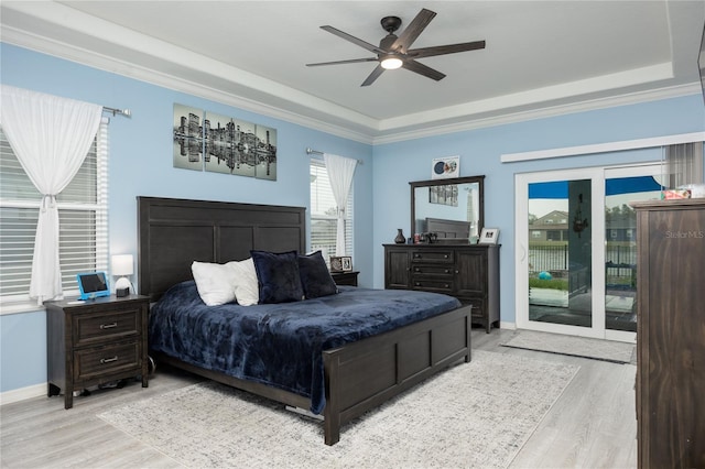 bedroom featuring access to exterior, light wood-style floors, and a tray ceiling