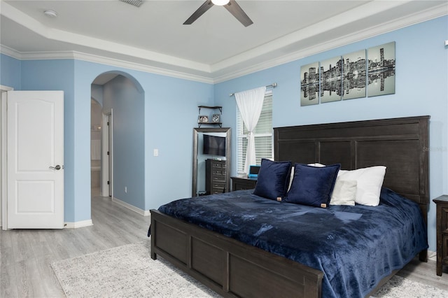 bedroom featuring crown molding, baseboards, a tray ceiling, light wood-style flooring, and arched walkways