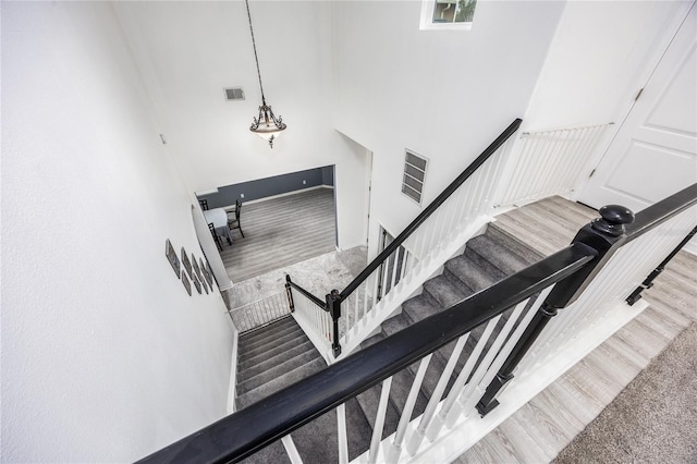 stairway with a high ceiling, wood finished floors, and visible vents