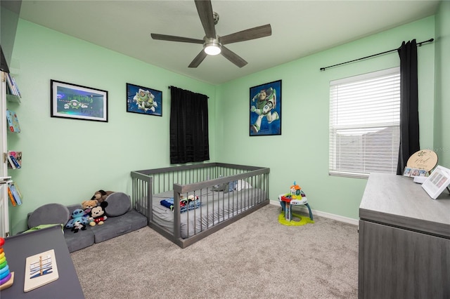 carpeted bedroom with baseboards, a crib, and ceiling fan