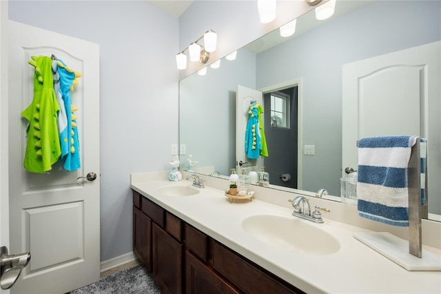 full bathroom featuring double vanity, baseboards, and a sink