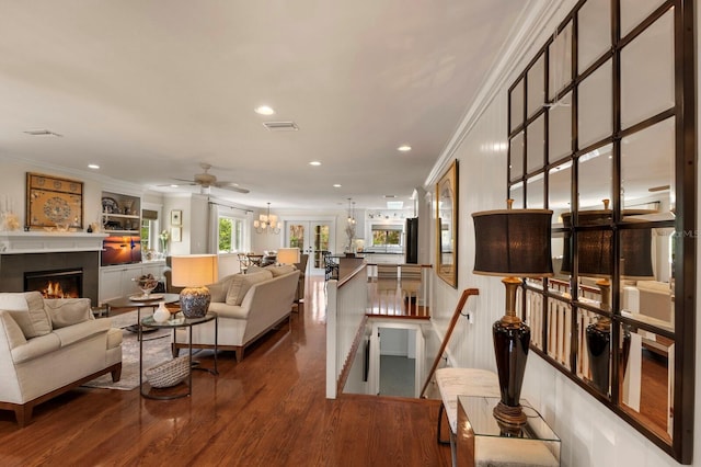 living area featuring visible vents, a notable chandelier, a warm lit fireplace, wood finished floors, and crown molding