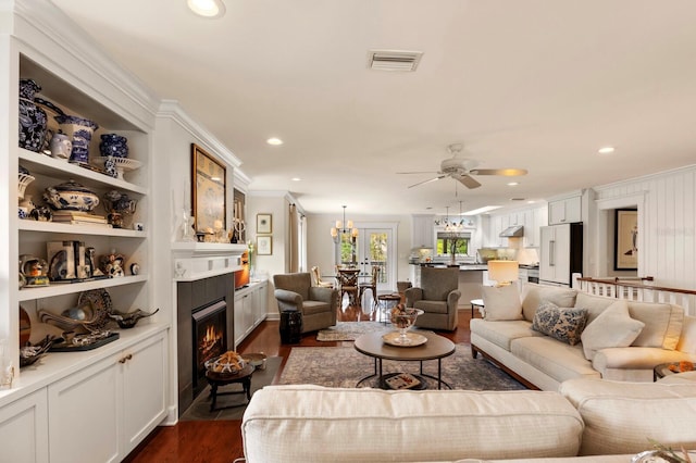 living room with built in shelves, visible vents, a fireplace with flush hearth, dark wood-style flooring, and ornamental molding