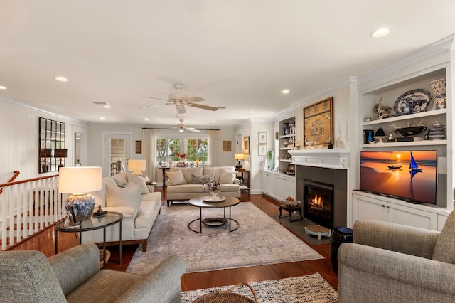 living room with a glass covered fireplace, built in shelves, dark wood-style floors, and ornamental molding