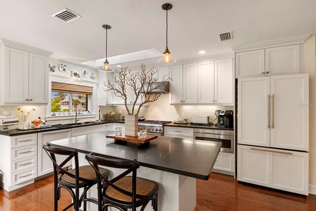 kitchen with dark countertops, visible vents, premium appliances, white cabinetry, and a sink