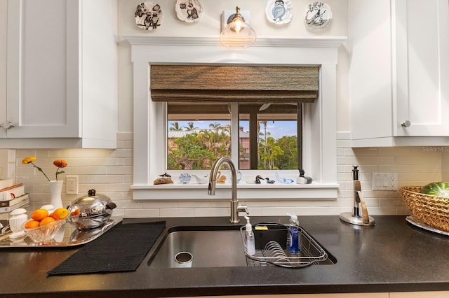 kitchen with a sink, tasteful backsplash, dark countertops, and white cabinets