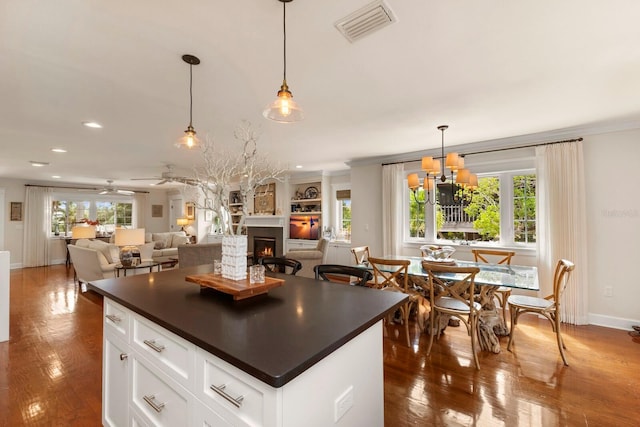 kitchen featuring dark countertops, visible vents, a healthy amount of sunlight, a lit fireplace, and hardwood / wood-style floors