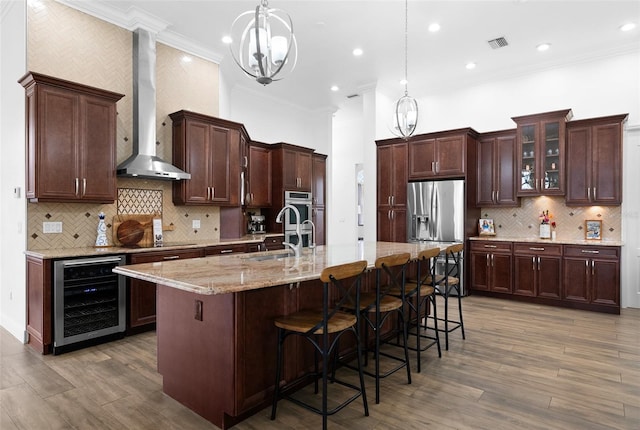 kitchen featuring visible vents, a sink, wine cooler, wall chimney range hood, and stainless steel fridge