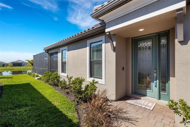 property entrance with a yard, a water view, and stucco siding