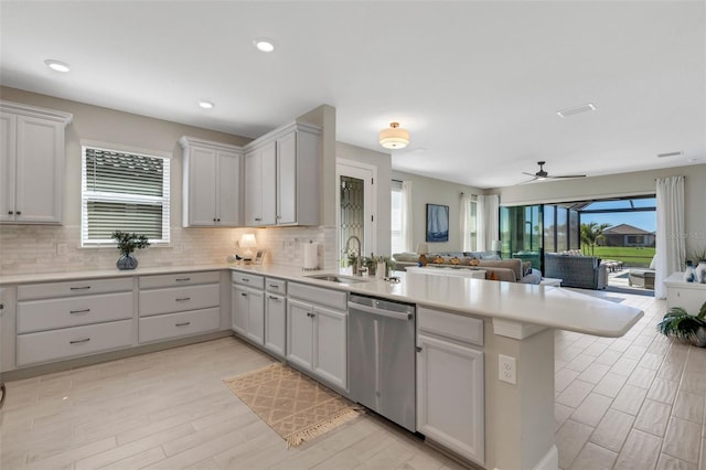 kitchen with open floor plan, light countertops, a peninsula, stainless steel dishwasher, and a sink