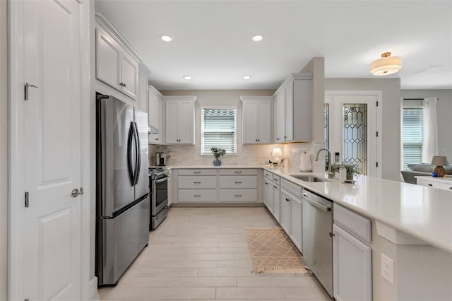 kitchen featuring a peninsula, a sink, stainless steel appliances, light countertops, and backsplash