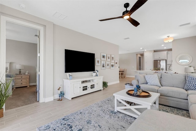 living room with a ceiling fan, light wood-style flooring, baseboards, and visible vents