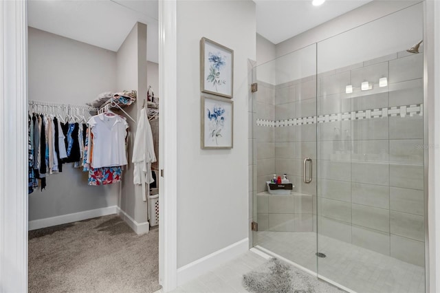 bathroom featuring a walk in closet, baseboards, and a stall shower