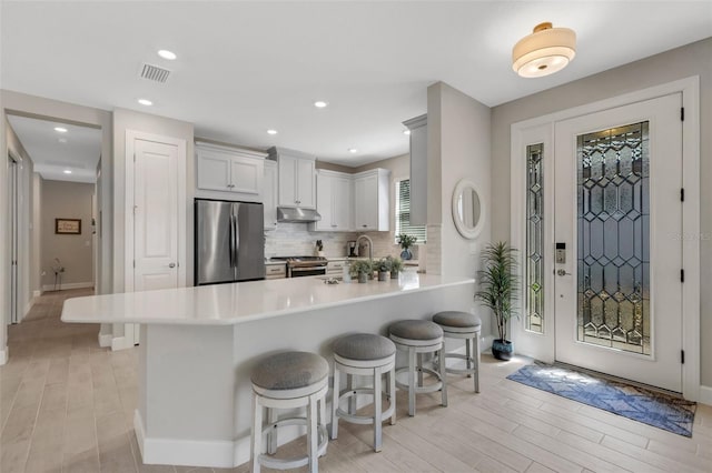 kitchen with visible vents, stainless steel appliances, decorative backsplash, under cabinet range hood, and a kitchen bar