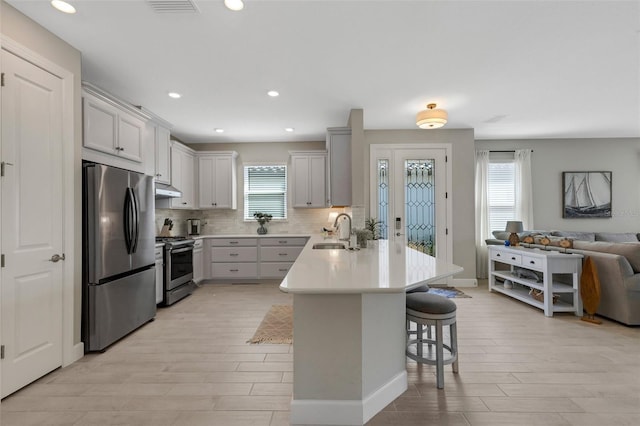 kitchen featuring open floor plan, a kitchen bar, a peninsula, stainless steel appliances, and a sink