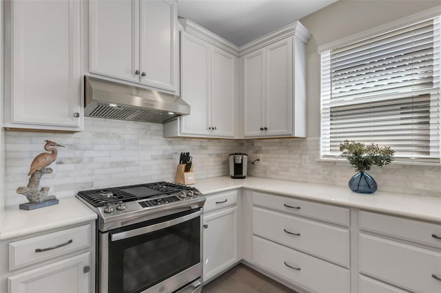 kitchen with light countertops, white cabinets, under cabinet range hood, stainless steel gas stove, and backsplash