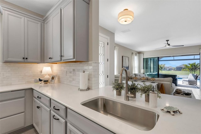 kitchen with tasteful backsplash, open floor plan, light countertops, a ceiling fan, and a sink