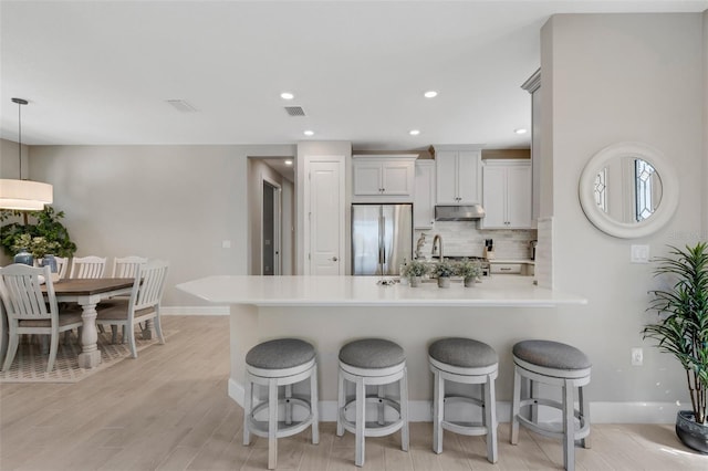 kitchen featuring a peninsula, a kitchen breakfast bar, under cabinet range hood, and stainless steel refrigerator