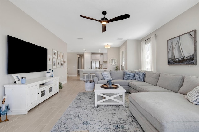 living area featuring ceiling fan, baseboards, and light wood-style floors