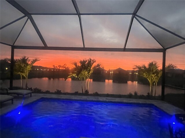 pool at dusk with a patio, an outdoor pool, a water view, and a lanai