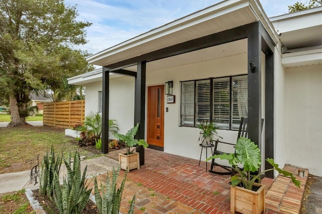 entrance to property featuring stucco siding and fence