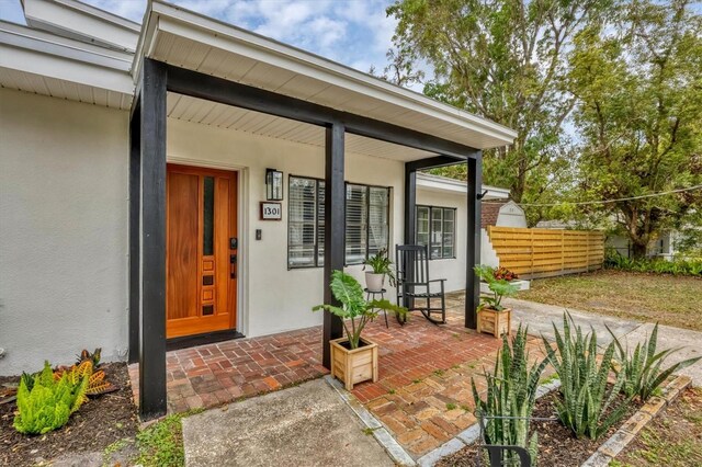 doorway to property featuring stucco siding, covered porch, and fence