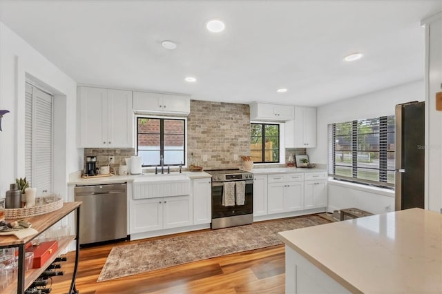 kitchen with light wood-type flooring, a sink, stainless steel appliances, white cabinets, and light countertops