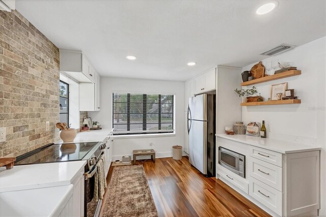 kitchen with visible vents, stainless steel appliances, wood finished floors, white cabinetry, and open shelves