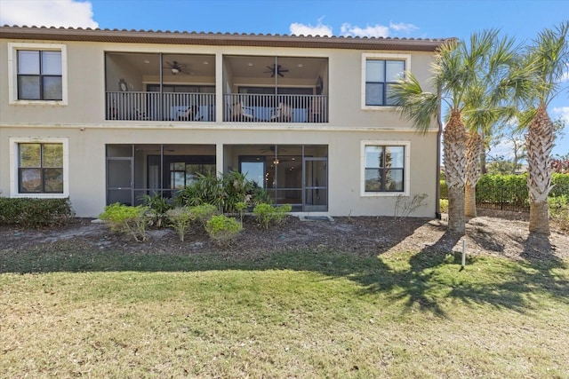 rear view of property featuring stucco siding, a balcony, ceiling fan, and a yard