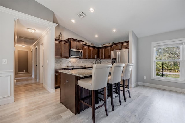 kitchen featuring tasteful backsplash, visible vents, a kitchen bar, lofted ceiling, and stainless steel appliances