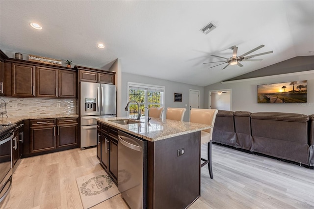 kitchen with visible vents, a kitchen bar, vaulted ceiling, appliances with stainless steel finishes, and a sink