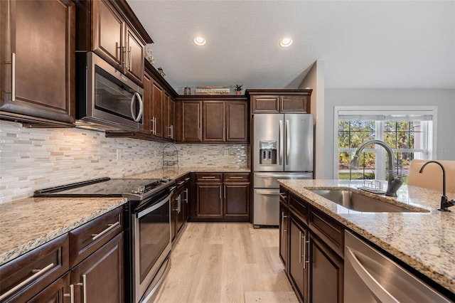 kitchen with a sink, light stone counters, stainless steel appliances, dark brown cabinetry, and light wood-style floors