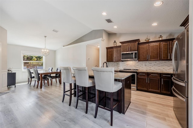 kitchen with visible vents, a center island with sink, lofted ceiling, appliances with stainless steel finishes, and a kitchen breakfast bar