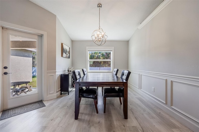 dining area with lofted ceiling, a wainscoted wall, light wood finished floors, and a chandelier