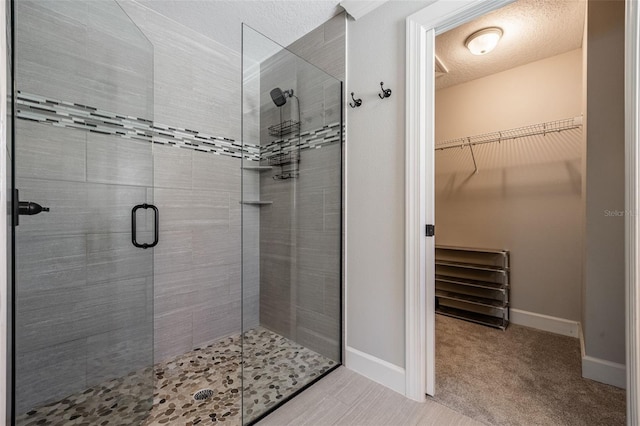 bathroom with a spacious closet, baseboards, a stall shower, and a textured ceiling