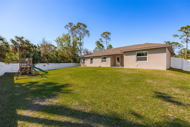 rear view of property with a playground, a fenced backyard, a lawn, and stucco siding