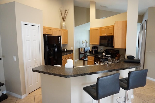 kitchen with light tile patterned flooring, light brown cabinets, black appliances, and a peninsula