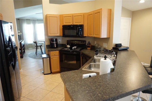 kitchen with dark countertops, light brown cabinets, a peninsula, black appliances, and a sink