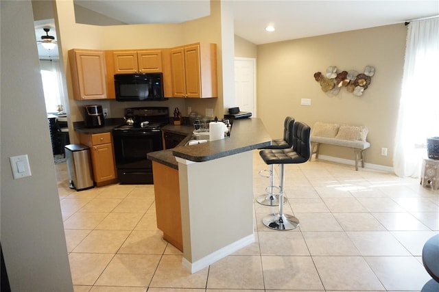 kitchen with a peninsula, light tile patterned flooring, black appliances, dark countertops, and a kitchen breakfast bar