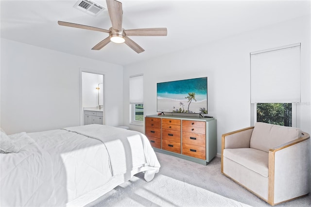 bedroom with a ceiling fan, visible vents, ensuite bathroom, multiple windows, and light colored carpet