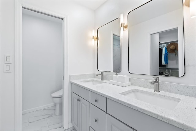 bathroom featuring double vanity, marble finish floor, toilet, and a sink