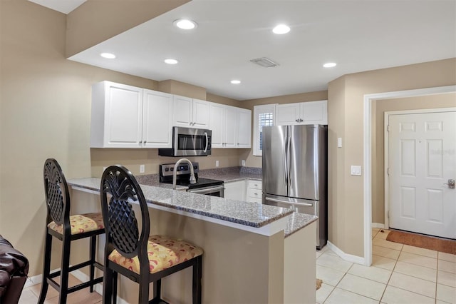 kitchen with light stone counters, recessed lighting, a peninsula, stainless steel appliances, and white cabinetry