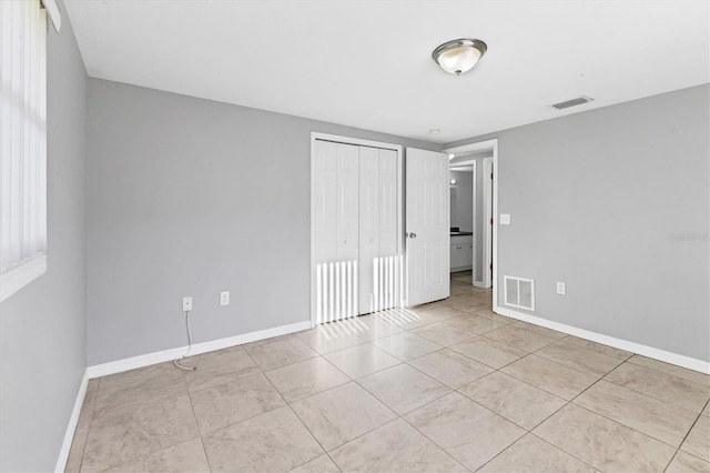 unfurnished bedroom featuring light tile patterned flooring, baseboards, visible vents, and a closet