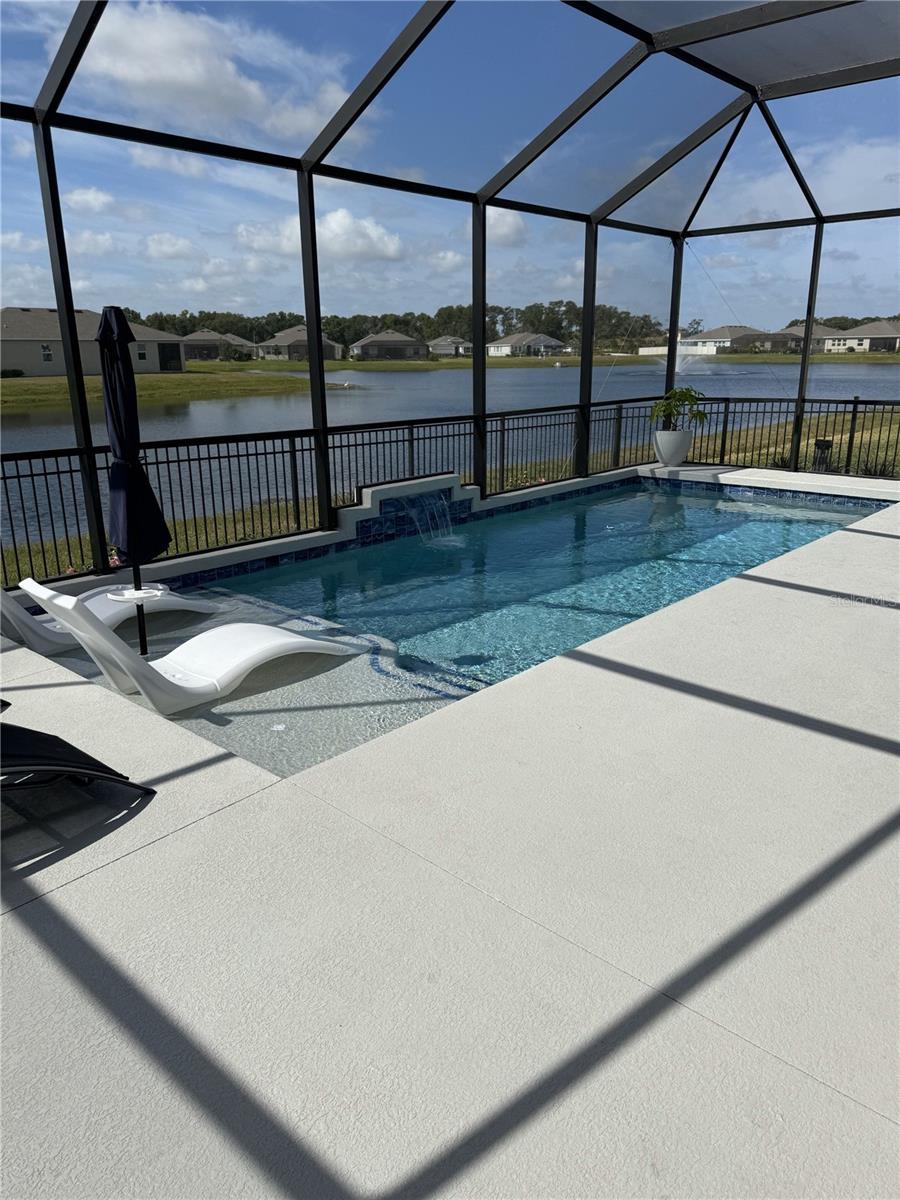 view of swimming pool featuring a patio area, glass enclosure, a water view, and a fenced in pool