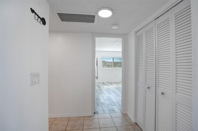 corridor featuring light tile patterned floors, visible vents, a textured ceiling, and baseboards