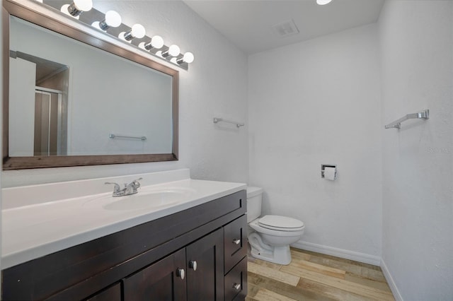 bathroom featuring baseboards, toilet, a stall shower, wood finished floors, and vanity