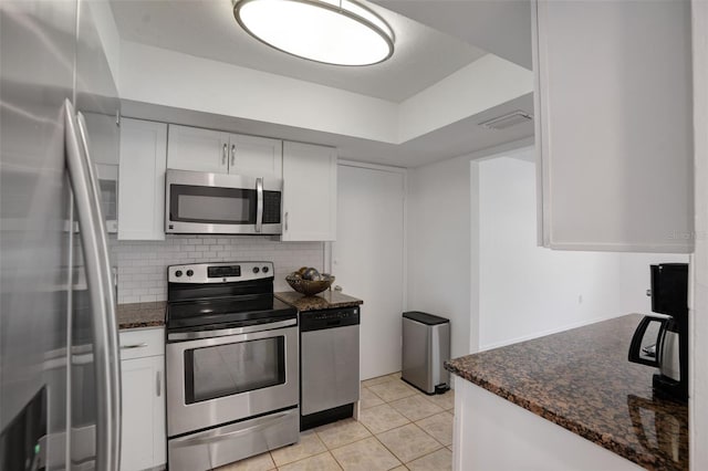 kitchen featuring backsplash, dark stone countertops, light tile patterned flooring, white cabinets, and stainless steel appliances