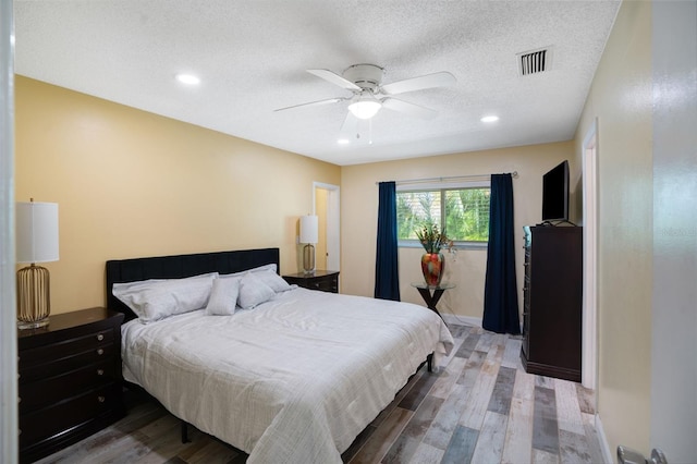 bedroom featuring a ceiling fan, wood finished floors, visible vents, and a textured ceiling