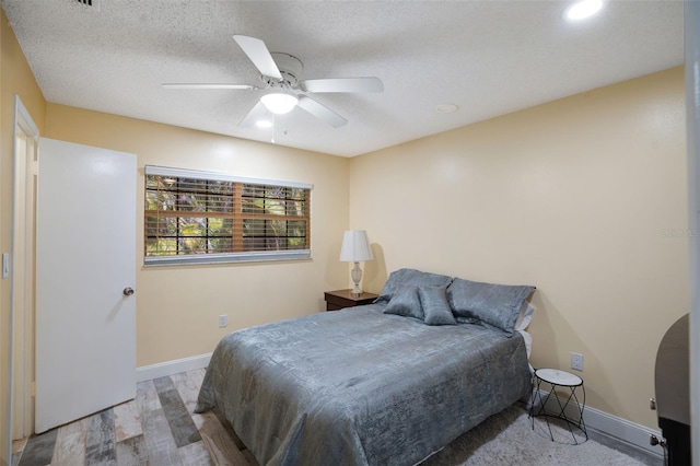 bedroom featuring a ceiling fan, wood finished floors, baseboards, and a textured ceiling