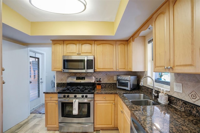 kitchen with a sink, appliances with stainless steel finishes, dark stone countertops, and light brown cabinets